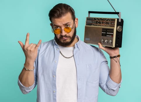 Young lebanese man using retro tape record player to listen music, disco dancing of favorite track, having fun, entertaining, fan of vintage technologies. Arabian guy isolated on blue background