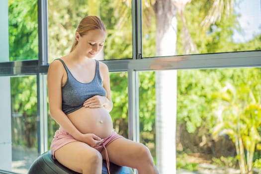 Pregnant woman exercising on fitball at home. Pregnant woman doing relax exercises with a fitness pilates ball. Against the background of the window.