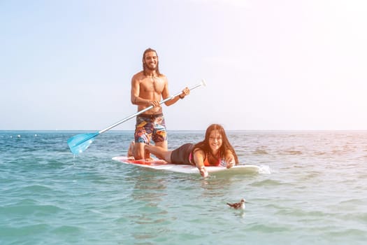 Silhouette of woman standing, surfing on SUP board, confident paddling through water surface. Idyllic sunset or sunrise. Sports active lifestyle at sea or river.