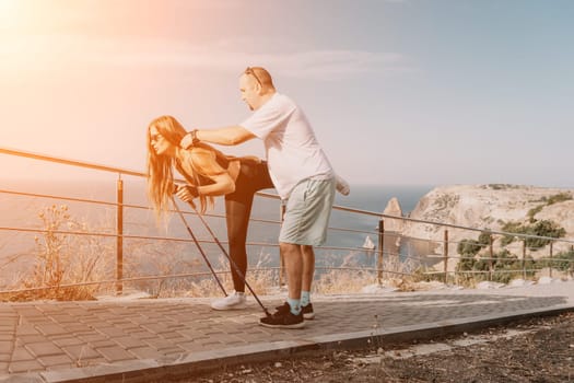 Happy Middle aged couple or friends practicing nordic walking in park near sea. Mature couple with trekking poles walking, practicing Nordic walking outdoors. Aging youthfully and sport concept.