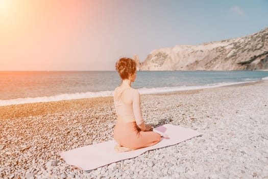 Middle aged well looking woman with black hair doing Pilates with the ring on the yoga mat near the sea on the pebble beach. Female fitness yoga concept. Healthy lifestyle, harmony and meditation.