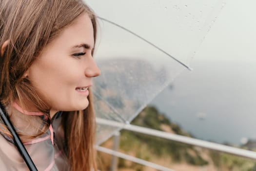 Woman rain park. Happy woman portrait wearing a raincoat with transparent umbrella outdoors on rainy day in park near sea. Girl on the nature on rainy overcast day