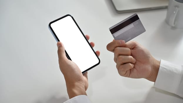 Hand holding credit card and using smartphone for online shopping, e-commerce or internet banking.