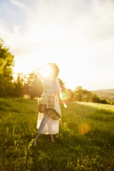 a woman in a light dress is happily spinning in nature, holding a hat in her hands, illuminated from the back by the sun. High quality photo