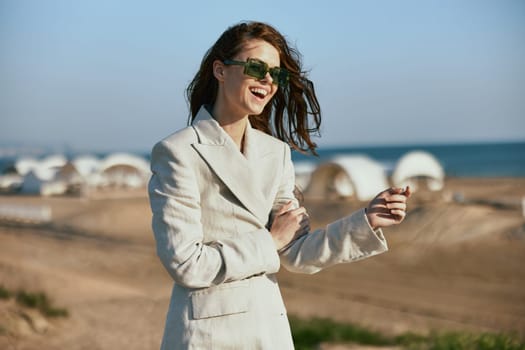 stylish woman with red hair standing on the coast in sunglasses laughing. High quality photo