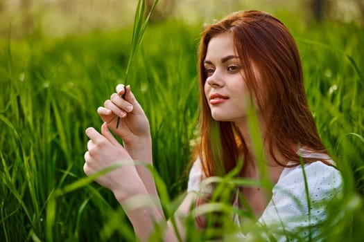 pensive woman with red hair sits in tall grass. High quality photo