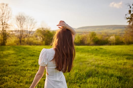 photo from the back of a red-haired woman raising her hands in happiness with a bouquet of flowers in the rays of the setting sun. High quality photo