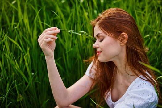 portrait of a beautiful redhead woman sitting in the grass on a sunny day at sunset. High quality photo