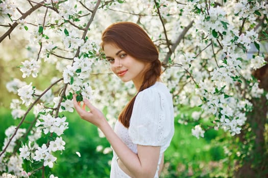 a beautiful woman in a light dress enjoys the spring while standing next to a flowering tree. High quality photo