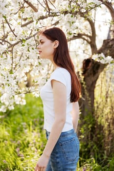 portrait of a happy woman with red hair in casual clothes enjoying the flowering of a fruit tree. High quality photo