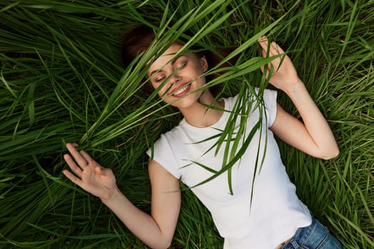 happy woman lies in high grass biting leaves with beautiful, even teeth. High quality photo