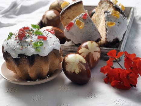 A cut Easter homemade Easter cake, eggs and a flower are laid out on a white natural tablecloth.