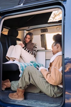two young friends reading and relaxing together during a road trip in camper van, concept of travel and adventure with best friend
