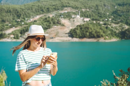 Woman texting online on mobile phone of mountains lake background. Traveler female chat messages on cellphone on the blue lake outdoors travel adventure vacation. Using smartphone