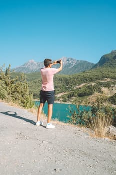 Man shooting a video on mobile phone of mountains lake background. Traveler male taking photo on cellphone on the blue lake outdoors travel adventure vacation.