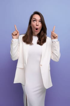 surprised young brunette woman in white dress pointing her finger to the side.