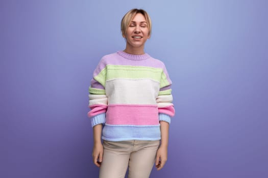 smiling blond woman in casual striped sweater on purple background.