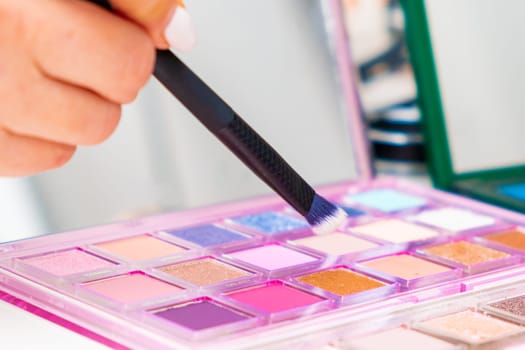 Close up makeup artist uses a brush to pick up eyeshadow from the palette