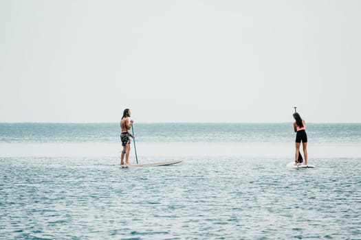 Sea woman and man on sup. Silhouette of happy young woman and man, surfing on SUP board, confident paddling through water surface. Idyllic sunset. Active lifestyle at sea or river