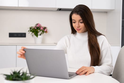 Young beautiful woman sits at her workplace and opens the laptop for working online. Freelance working at home.