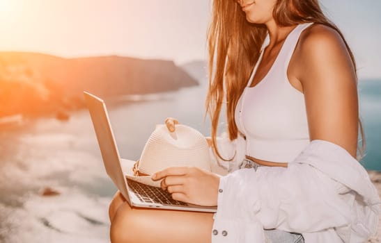 Digital nomad, Business woman working on laptop by the sea. Pretty lady typing on computer by the sea at sunset, makes a business transaction online from a distance. Freelance remote work on vacation