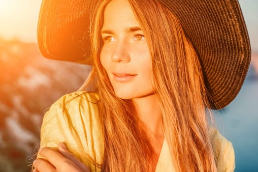 Portrait of happy young woman wearing summer black hat with large brim at beach on sunset. Closeup face of attractive girl with black straw hat. Happy young woman smiling and looking at camera at sea