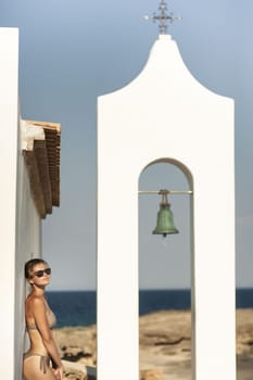 Young woman in a swimsuit on the background of Greek architecture and the sea. Woman in sexy bikini and santoini landscape.