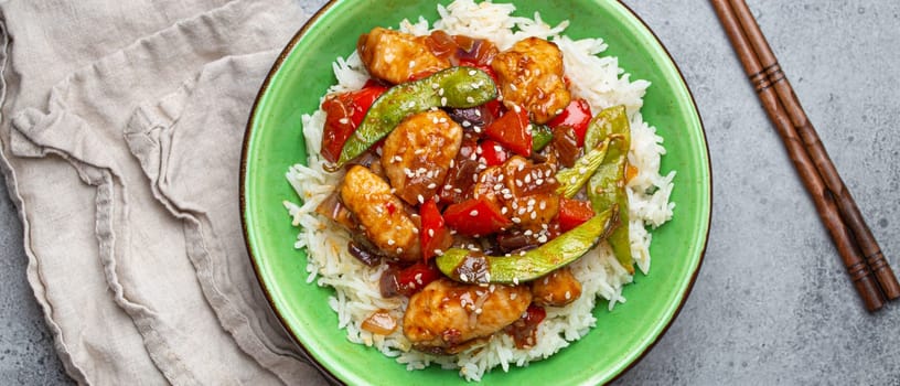 Asian sweet and sour sticky chicken with vegetables stir-fry and rice in ceramic bowl with chopsticks top view on gray rustic stone background, traditional Asian dish