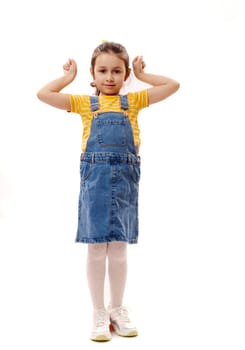 Full length vertical portrait of Caucasian lovely little child girl gesturing, clenching fists, looking at camera, isolated over white background