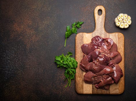 Raw chicken liver on wooden cutting board top view on dark rustic concrete background kitchen table. Healthy food ingredient, source of iron, folate, vitamins and minerals. Space for text