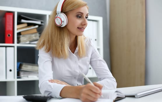 Woman in headphones at desk takes notes in documents. Remote learning or business conference