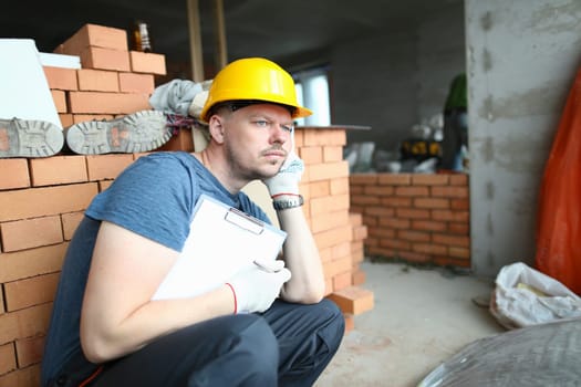 Thoughtful sad builder holding clipboard and looking into distance. Solving construction problem and builder depression