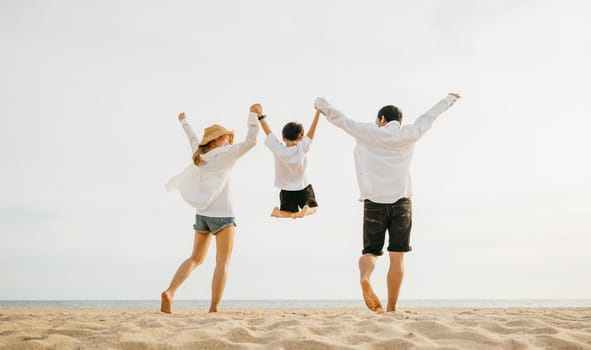 Back family mother, father and son holding hands and jumping in air at dawn time, Family outdoor activities, Happy Asian family people have fun healthy lifestyle together on beach, holiday vacation