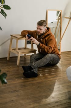 Freelance man using mobile phone checking social media network feed or message chat sitting on bed at home. Online digital communication rest after hard work day