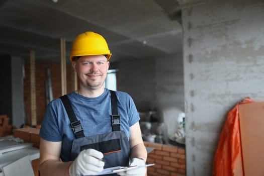 Smiling handsome male builder in hardhat holding pen and clipboard. Construction services and quality control of construction works