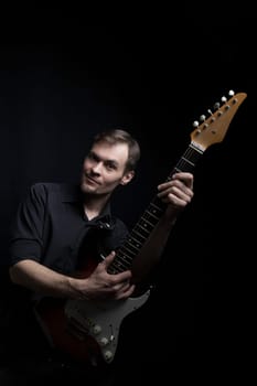 Caucasian man guitarist playing on electric guitar on black background.