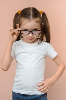Caucasian girl 7 years old in a white T-shirt and jeans with diopter eye glasses, vertical studio portrait.