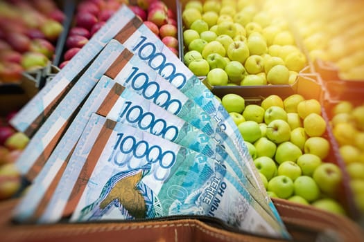 Rising prices for fruits and agricultural products in Kazakhstan. Tenge in a wallet against the background of a counter with apples.