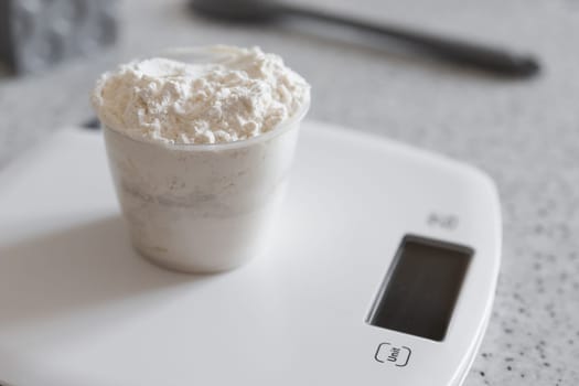Measuring cup with flour on a white kitchen scale.