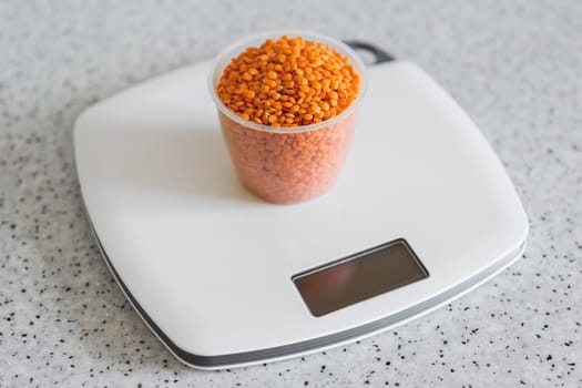 Lentils in a plastic measuring cup on an electronic kitchen scale.