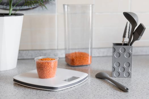 Healthy food or diet concept. Kitchen scale with measuring cup with lentils on the kitchen table.