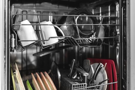 Close-up on open dishwasher machine with dishes built into the kitchen.