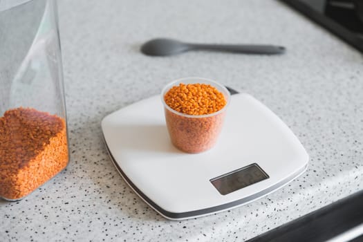 Red split lentils in a measuring cup on white digital scale displaying.
