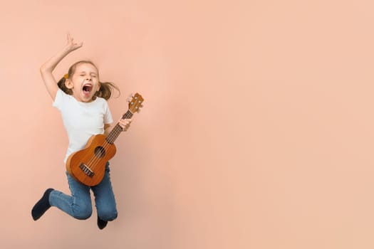 Emotional little jumping girl playing ukulele like rock star on pink background, copy space.