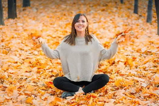Smiling young woman having fun in autumn park getting ready throws up tellow fallen leaves.