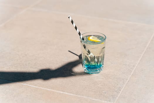 Closeup shot of hand's shadow holding sparkling mint lemonade tropical cocktail from the glass standing on the marble floor. Hello summer holiday vacation. Copy blank space.