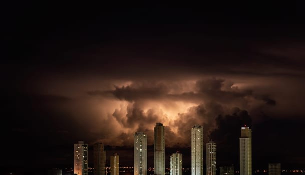 Dramatic orange storm clouds break through the night sky and hover over a city skyline of towering skyscrapers, creating a stunning contrast between light and dark. Copy space available.