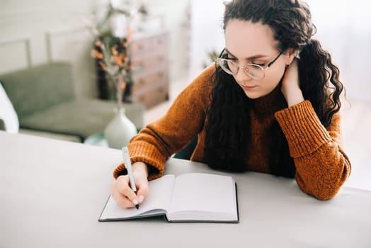 Woman writing in copybook. Business woman or young female student holding pen in hand writing in paper notebook journal, taking notes studying, doing homework, making checklist. Close up view.