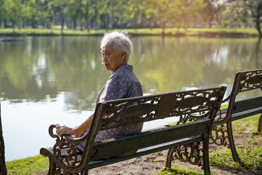 Asian elderly woman depressed and sad sitting back on bench in autumn park.