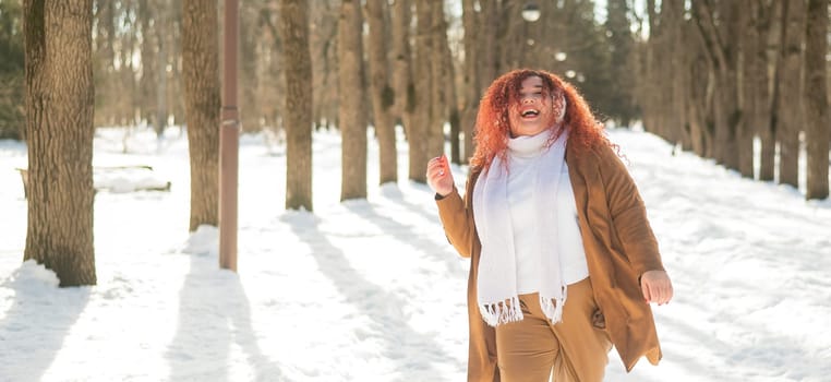 A fat woman listens to music with headphones and dances in the park in winter